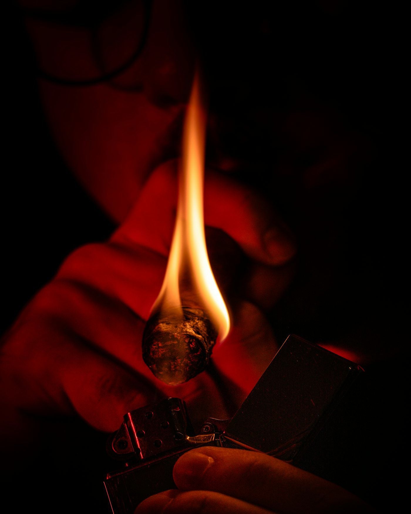 Close-up of a lit lighter with flames and cigar against a dark background
