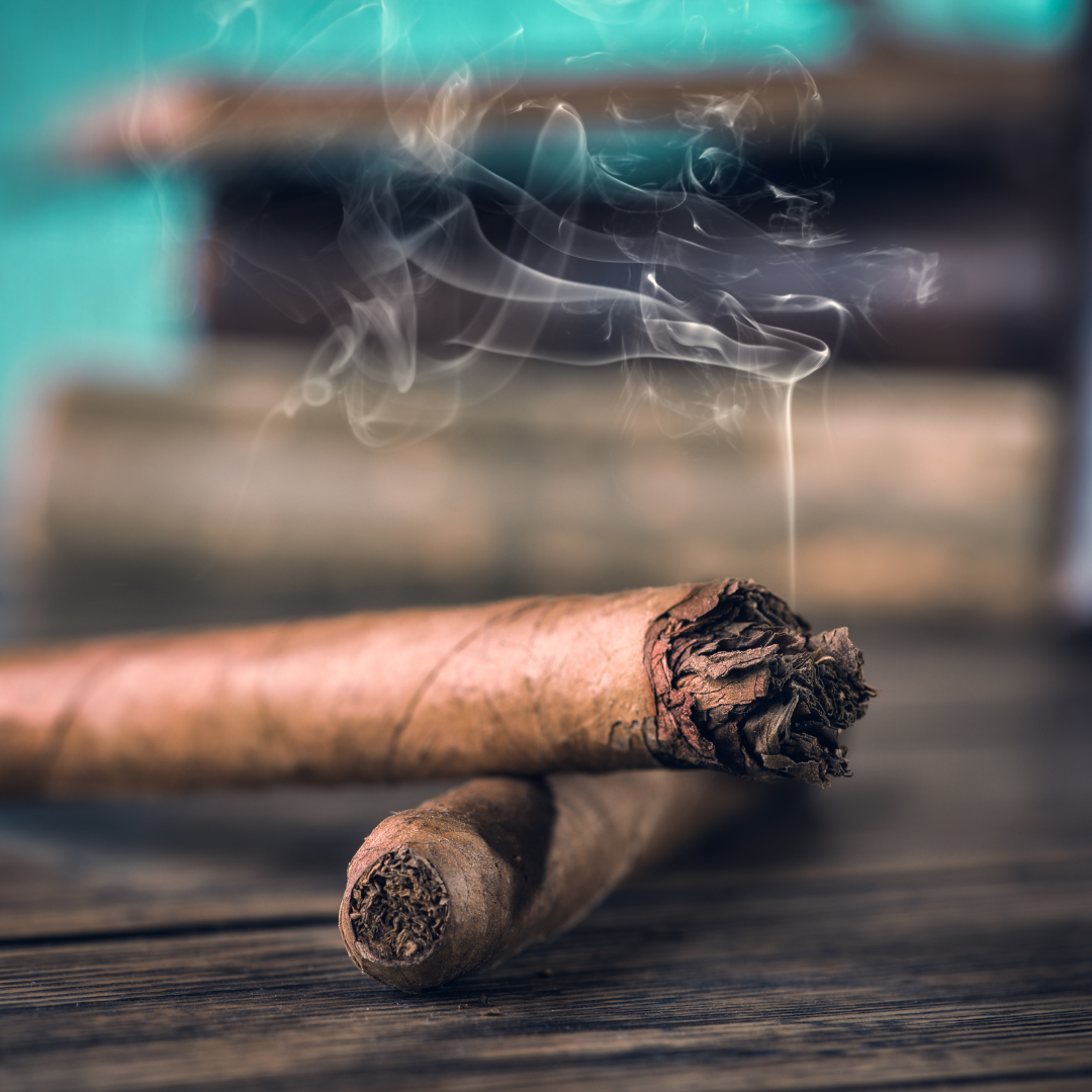 Two cigars with smoke rising from them on a wooden surface.